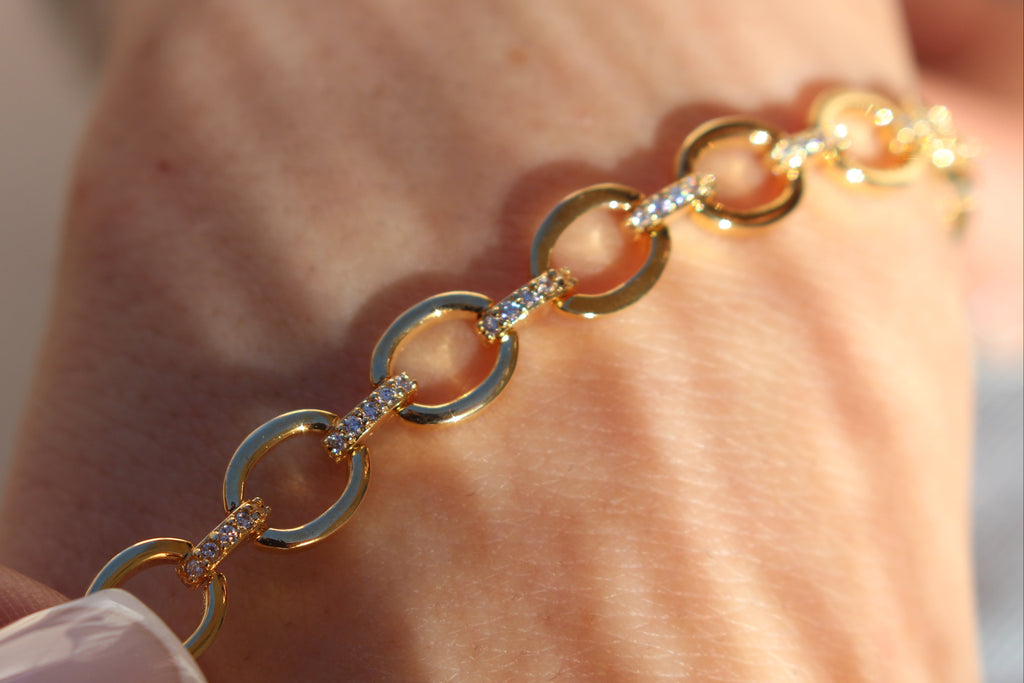 Gold bracelet with diamond accents on a wrist against a neutral background